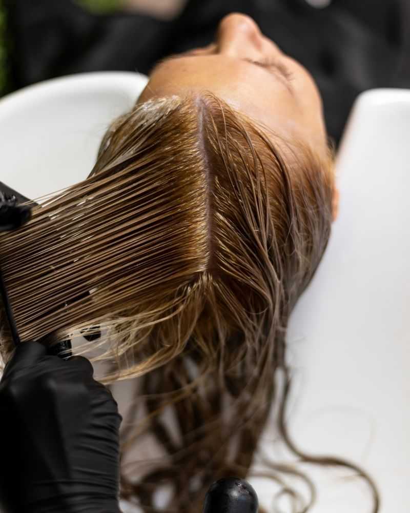 Hairdresser applying hair dye to a client's hair at a salon sink.